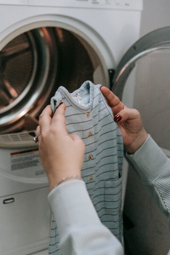 A person handles baby clothes next to a front-load washing machine indoors.